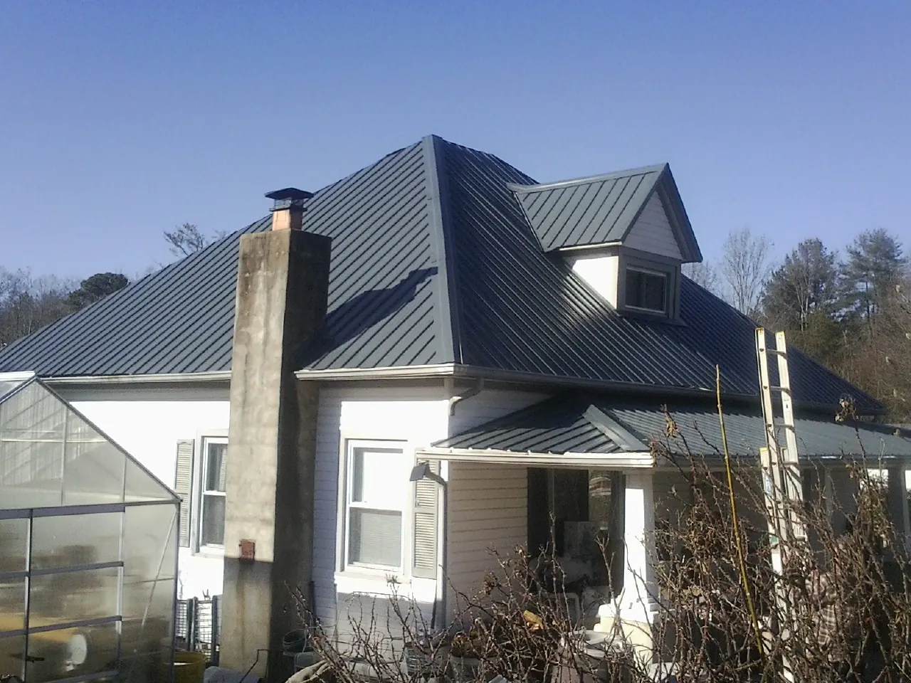 Dark blue standing seam metal roof on a white farmhouse with dormer — Slate & Tile Roof Repair by Roofing Brothers in Sasser