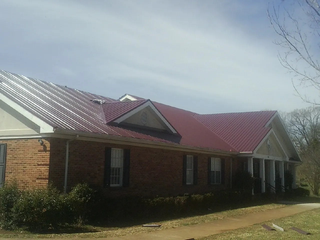 Red metal roof with gabled entries on a long brick building, from a Hail Damage Roof Repair job in Sasser