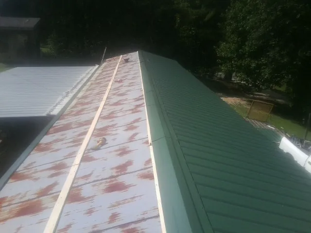 Old rusted panels beside newly installed green metal roofing — Wind Damage Roof Repair by Roofing Brothers in Sasser