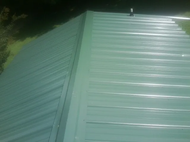 New green metal panels meeting at the ridge of a roof — Flat Roof Repair work by our crew in Sasser