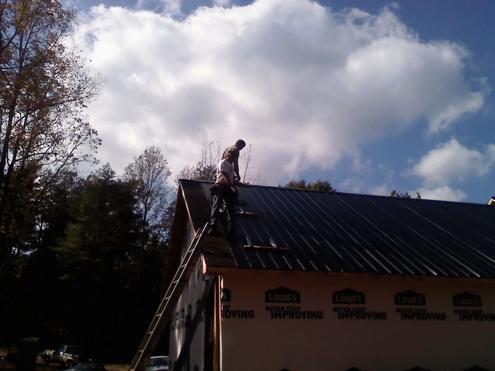 Roofer fastening dark metal panels high against a cloudy sky, from a Roof Inspection job in Sasser