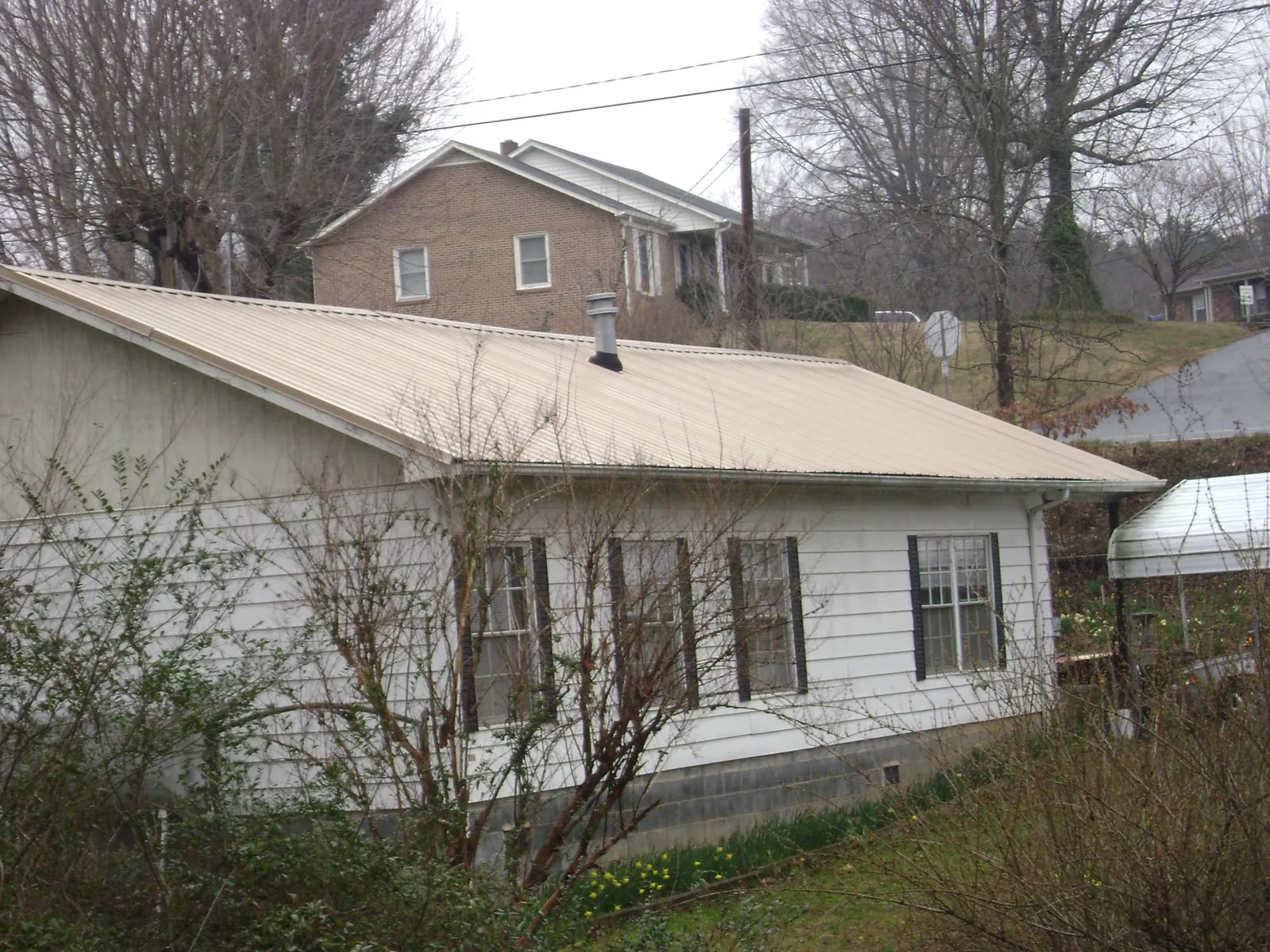 Tan metal roof on a white sided house set into a hillside — Commercial Roofing by Roofing Brothers in Sasser