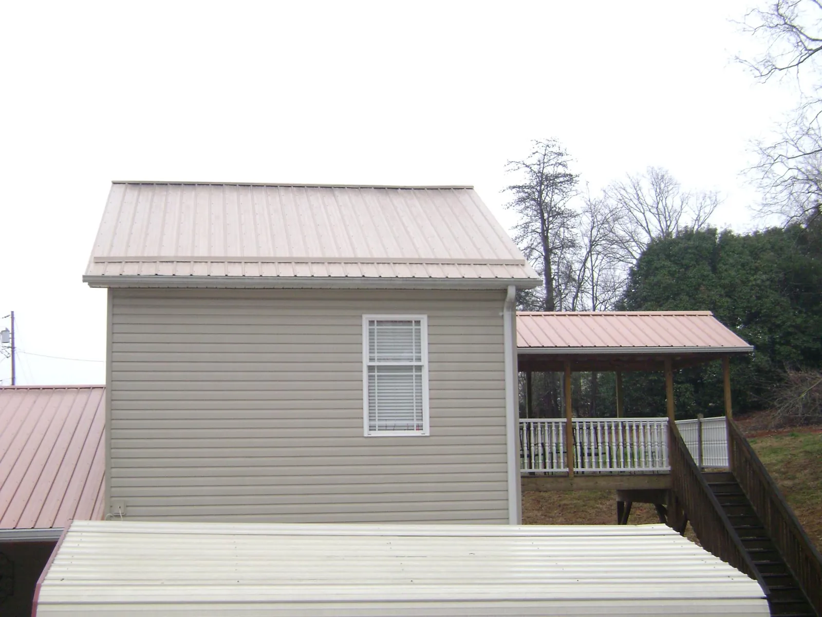 Tan metal roofs on a two story addition and attached porch, from a Roof Replacement job in Sasser